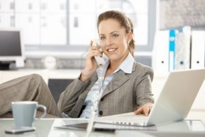 8251350-attractive-businesswoman-sitting-at-desk-talking-on-phone-having-laptop-smiling